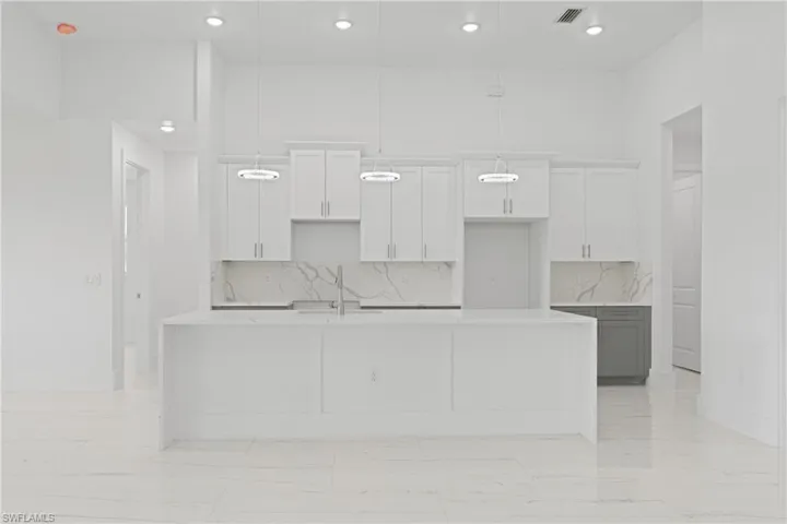 Kitchen featuring decorative backsplash, pendant lighting, a large island with sink, and light tile patterned floors