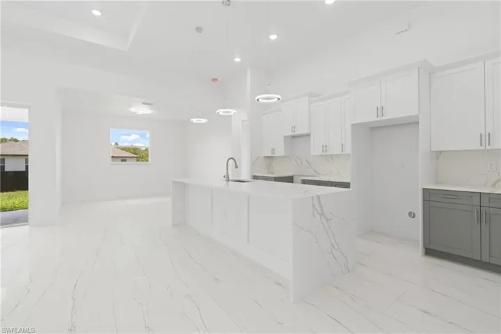 Kitchen featuring light stone counters, decorative backsplash, an island with sink, light tile patterned flooring, and white cabinetry