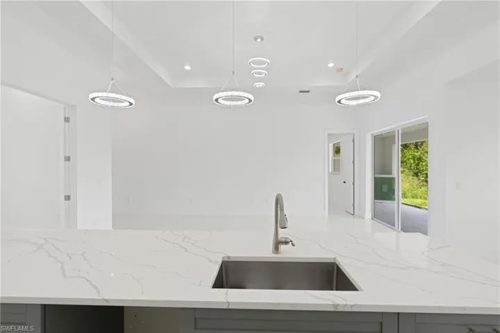 Kitchen with hanging light fixtures, sink, decorative backsplash, and light stone counters