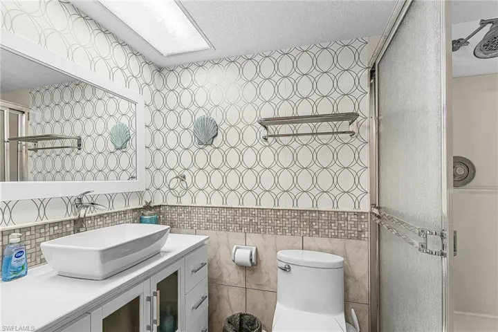 Full bath featuring tile walls, vanity, a stall shower, and a textured ceiling