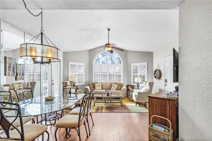 Dining room featuring lofted ceiling, a ceiling fan, wood finished floors, a chandelier, and a textured ceiling