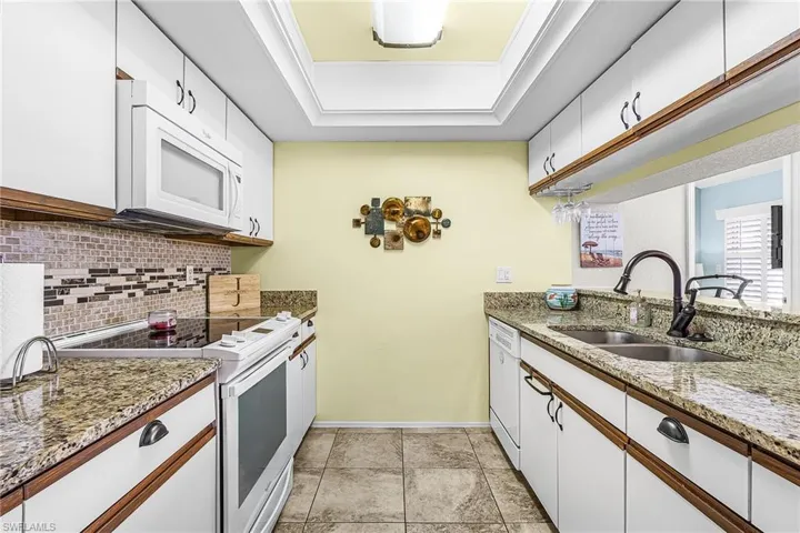 Kitchen featuring white appliances, white cabinets, light stone counters, decorative backsplash, and light tile floors