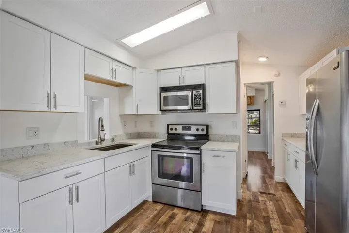 Kitchen featuring white cabinets, stainless steel appliances, dark hardwood / wood-style floors, and lofted ceiling