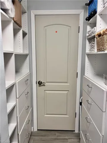 Spacious primary bedroom walk in closet with shelving, drawers and a wood finished floors