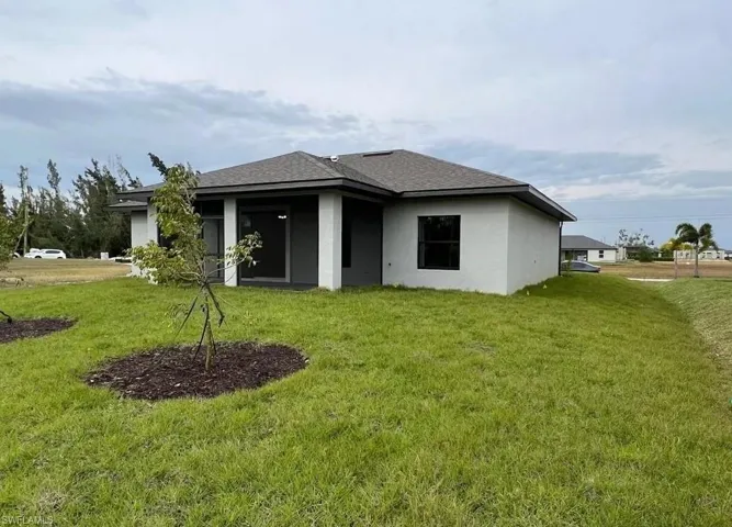 Rear view of property featuring a yard, stucco siding, roof with shingles, and a patio area