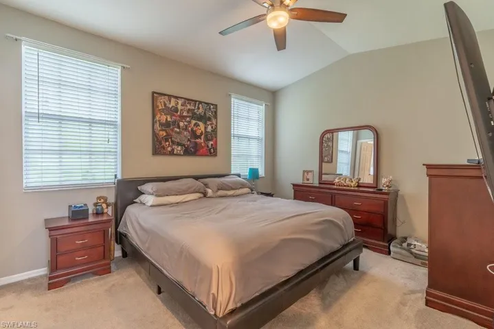 Carpeted bedroom featuring multiple windows, ceiling fan, and lofted ceiling