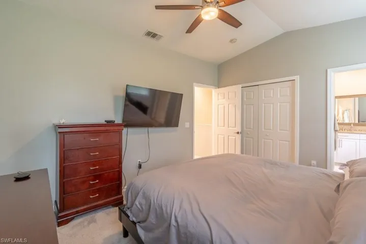 Carpeted bedroom with a closet, ceiling fan, and vaulted ceiling