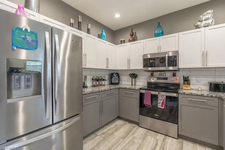 Kitchen featuring appliances with stainless steel finishes, tasteful backsplash, gray cabinets, and light stone counters