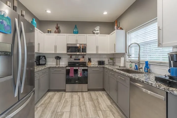 Kitchen with tasteful backsplash, white cabinets, sink, light stone counters, and appliances with stainless steel finishes
