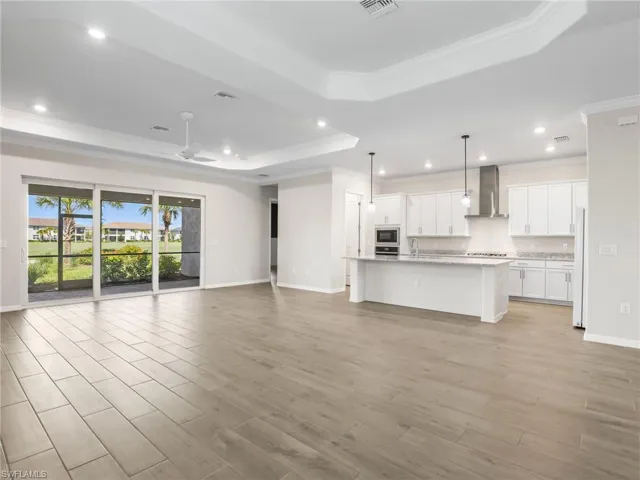 Great room with crown molding, a tray ceiling, recessed lighting, light wood-style tile flooring, and ceiling fan