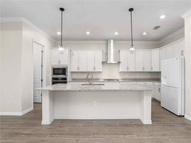 Kitchen featuring stainless steel appliances, wall range hood, tiled floors, a kitchen island with sink, and white cabinets