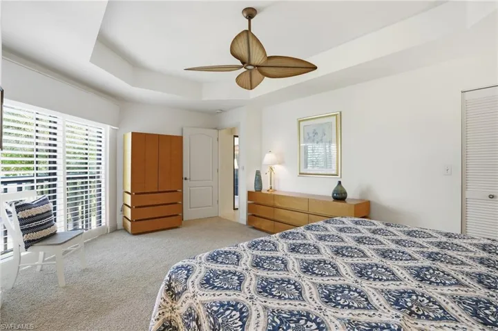 Bedroom with light colored carpet, a ceiling fan, a tray ceiling, and access to exterior