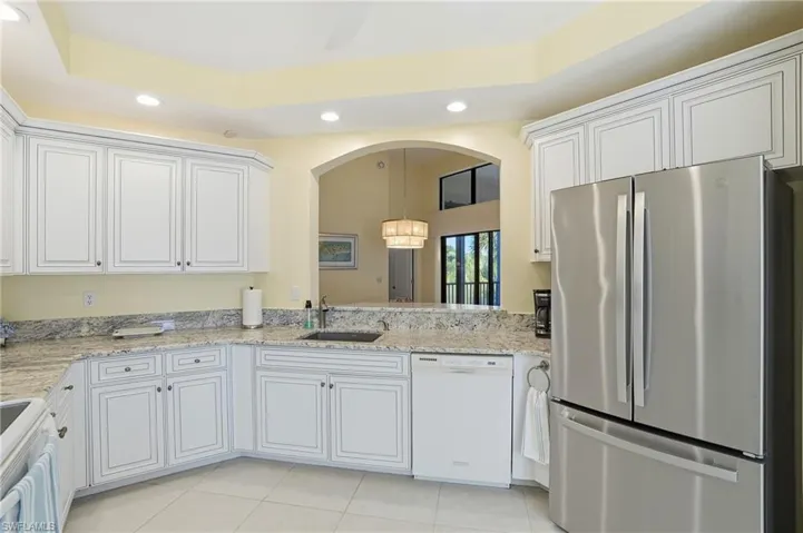 Kitchen featuring white appliances, a chandelier, recessed lighting, white cabinets, and light stone counters