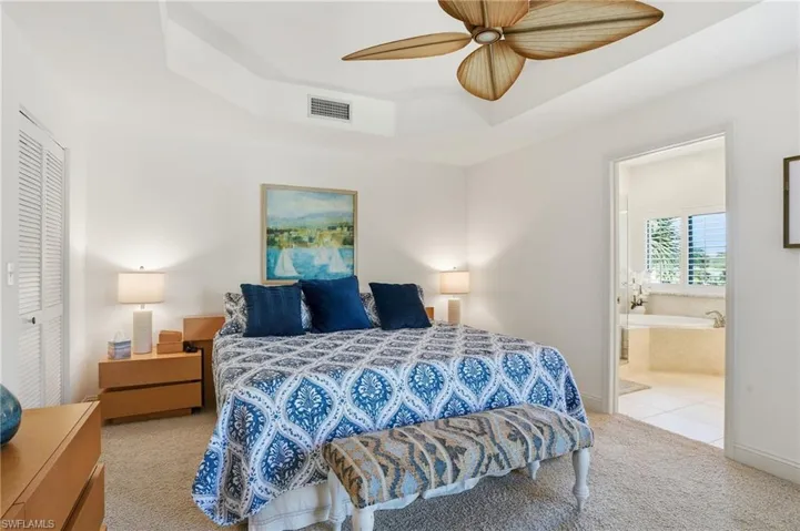 Bedroom with carpet floors, a raised ceiling, a ceiling fan, ensuite bathroom, and a closet