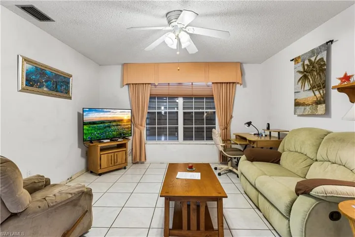 Living room featuring ceiling fan, a textured ceiling, and light tile floors