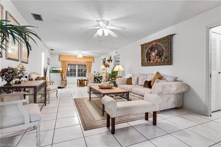 Living room with a textured ceiling, ceiling fan, and light tile floors
