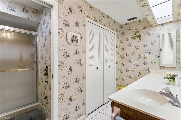 Bathroom with tile floors, a shower with shower door, a skylight, and vanity
