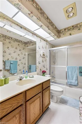Full bathroom with tile flooring, combined bath / shower with glass door, toilet, and vanity