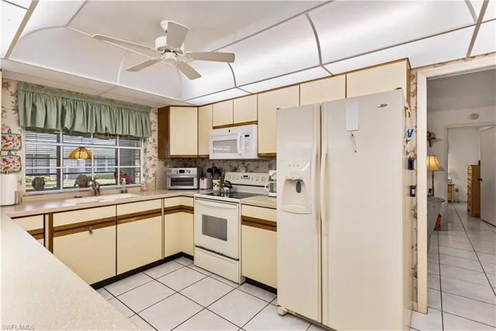 Kitchen with light tile floors, white appliances, ceiling fan, and cream cabinets