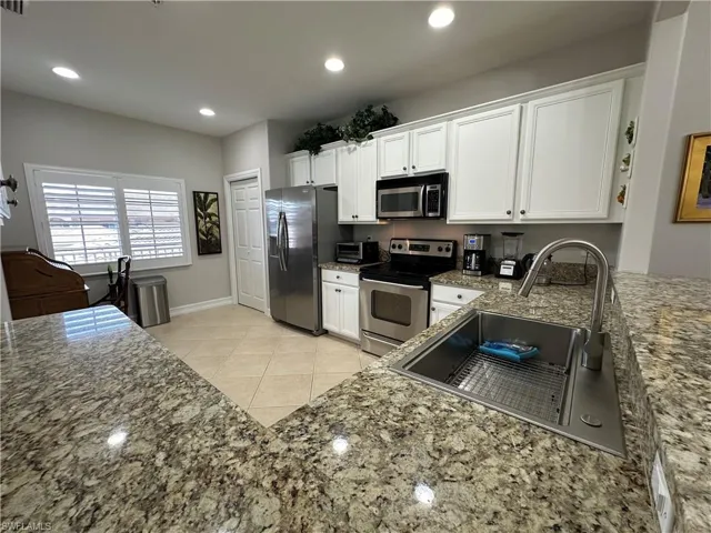 Kitchen featuring white cabinetry, light tile patterned floors, dark stone counters, appliances with stainless steel finishes, and sink