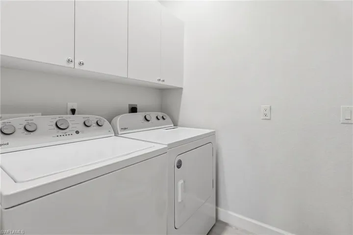 Laundry area featuring white cabinetry with silver-toned hardware, white appliances, and light-toned walls