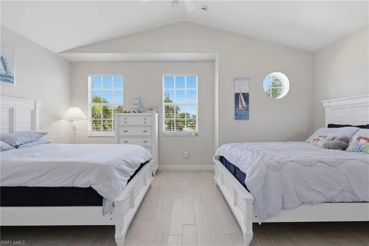 Bright bedroom featuring vaulted ceilings, light wood-finish flooring, two rectangular windows with blinds, and one circular window