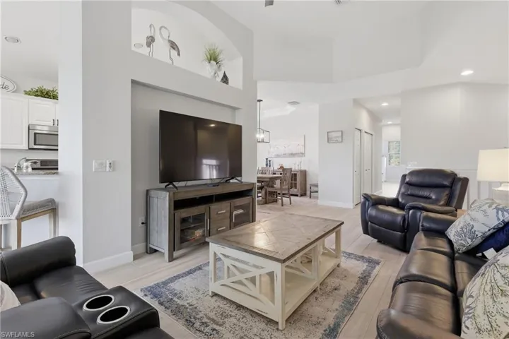 Open-concept living area featuring light wood-finish flooring, recessed lighting, and a tray ceiling