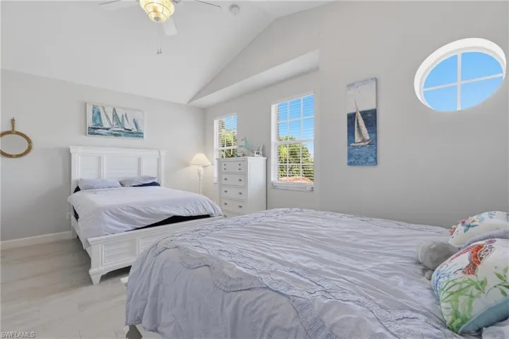 Vaulted ceiling room featuring light-toned wood-finish flooring, multiple windows including an oval-shaped window, and a ceiling fan with integrated lighting