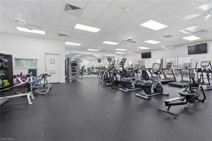 Spacious fitness room featuring extensive exercise equipment, rubberized flooring, ceiling fans, recessed lighting, and large exterior windows