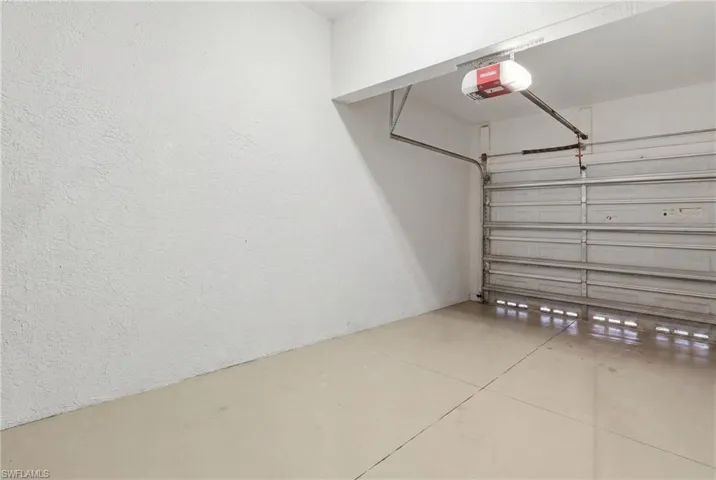 Single-car garage with a light-toned concrete floor, textured white walls, and an automatic garage door opener