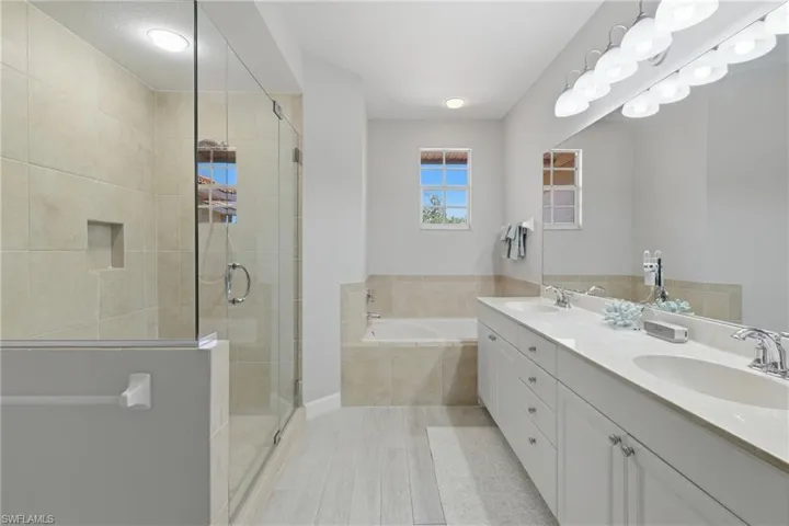 Spacious bathroom featuring a glass-enclosed shower with a built-in niche, a soaking tub with tile surround, a dual vanity with undermount sinks, and light wood-finish flooring