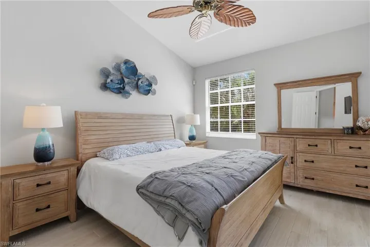 Vaulted ceiling bedroom featuring wood-finish flooring, a window with horizontal blinds, and a ceiling fan with palm leaf design blades