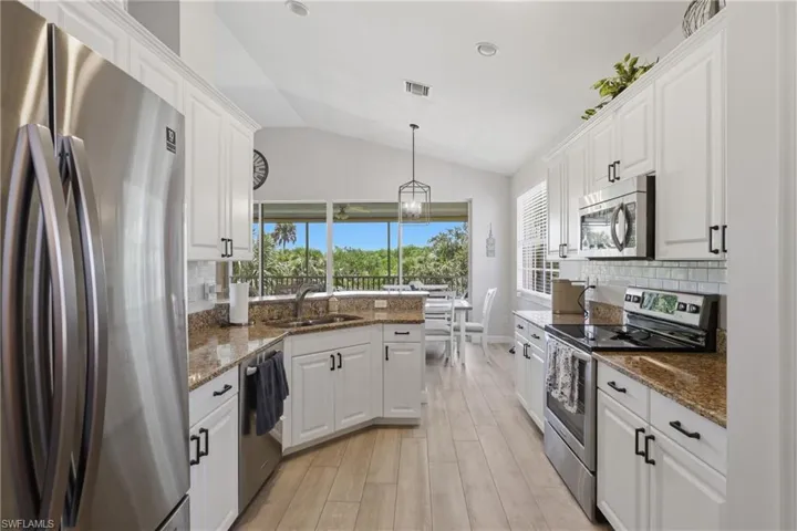 Modern kitchen featuring wood-finish flooring, white cabinetry with black hardware, stainless steel appliances, and light-toned countertops