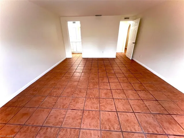 Spacious room featuring terra cotta tile flooring, white baseboards, and neutral wall tones