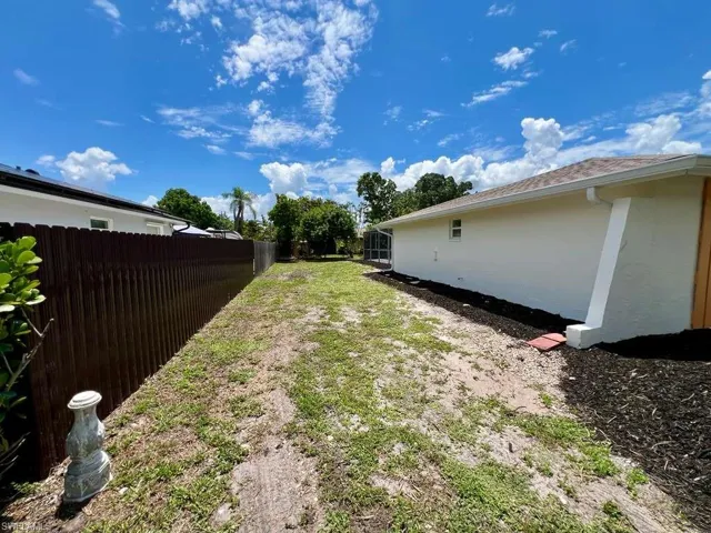 Expansive yard featuring a brown privacy fence, a stucco exterior, a shingle roof, and a landscaped bed with dark mulch