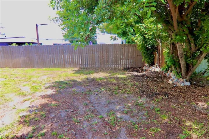 Expansive yard space featuring a perimeter wooden fence, mature trees, and natural ground cover