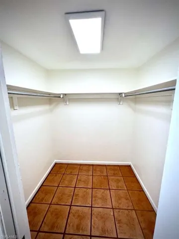 Recessed closet featuring ceramic tile flooring, white baseboards, a ceiling-mounted light fixture, and two clothing rods with shelving
