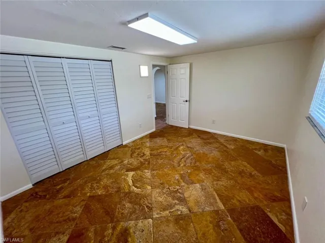 Spacious room featuring substantial tile flooring, louvered bi-fold closet doors, a rectangular overhead light fixture, a standard interior door with a paneled design, and a horizontal window with blinds