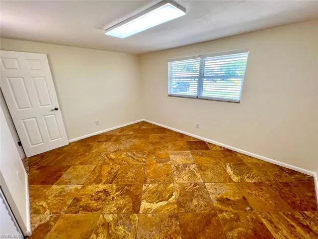 Spacious room featuring striking gold and brown patterned tile flooring, a window with horizontal blinds, a white six-panel door, and a flush-mount ceiling light fixture