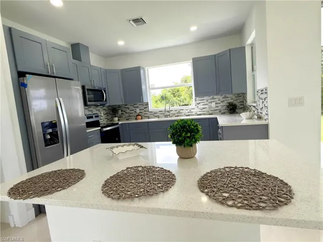 Kitchen featuring appliances with stainless steel finishes, backsplash, gray cabinets, light stone countertops, and recessed lighting