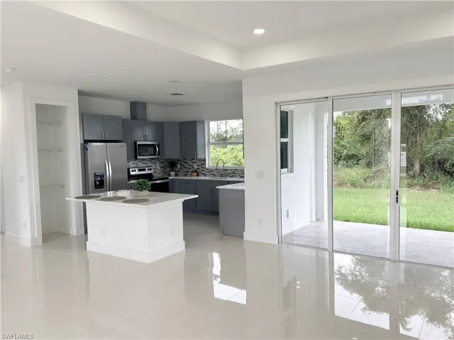 Kitchen with gray cabinetry, backsplash, a kitchen island, stainless steel appliances, and light tile patterned floors