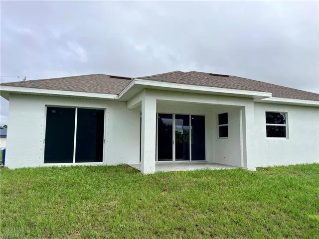Rear view of property with a patio, a yard, stucco siding, and roof with shingles