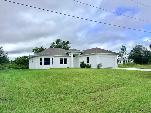 View of front of property with stucco siding, a front yard, driveway, a garage, and roof with shingles