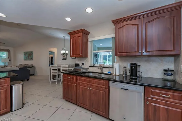 Kitchen featuring decorative light fixtures, decorative backsplash, sink, white dishwasher, and lofted ceiling