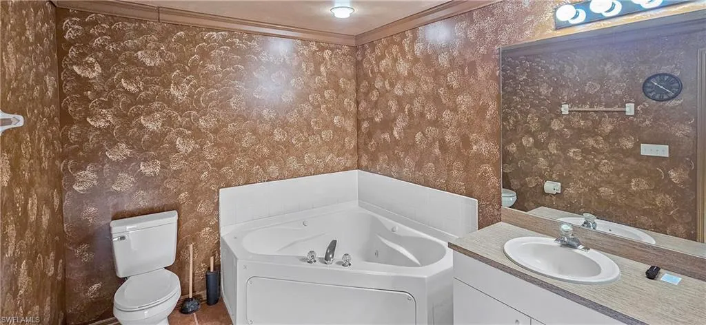 Bathroom featuring a jetted tub, vanity, and wallpapered walls