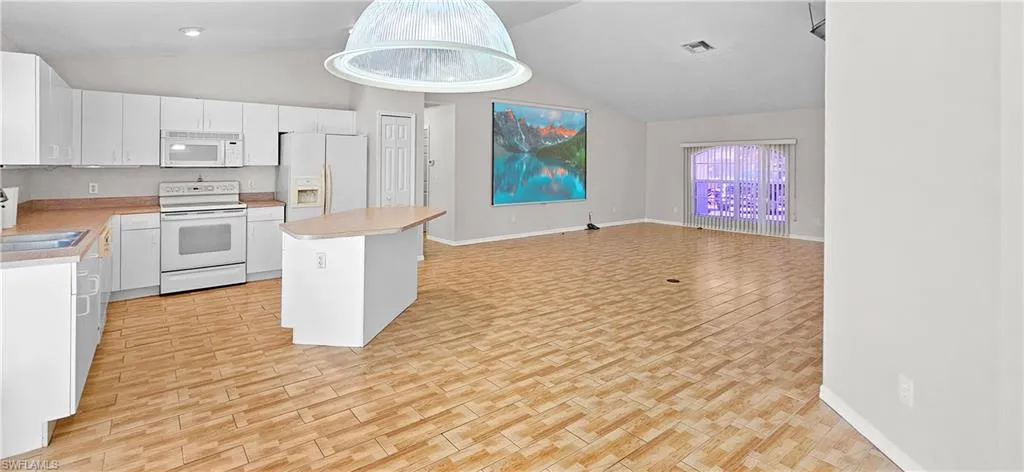 Kitchen with wood finish floors, white appliances, white cabinets, open floor plan, and light countertops
