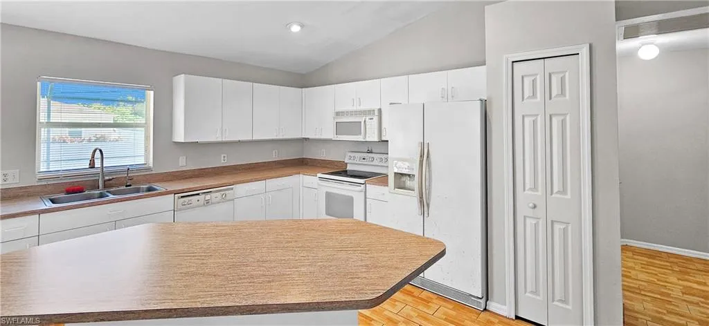 Kitchen featuring white appliances, white cabinets, lofted ceiling, light countertops, and light wood finished floors