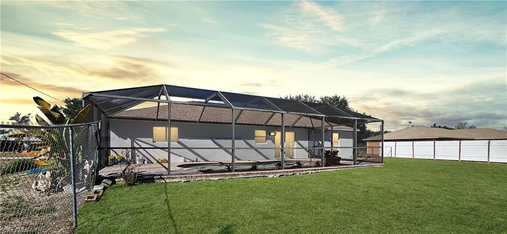 Back of house with a sunroom, a lanai, a fenced backyard, and an outdoor pool
