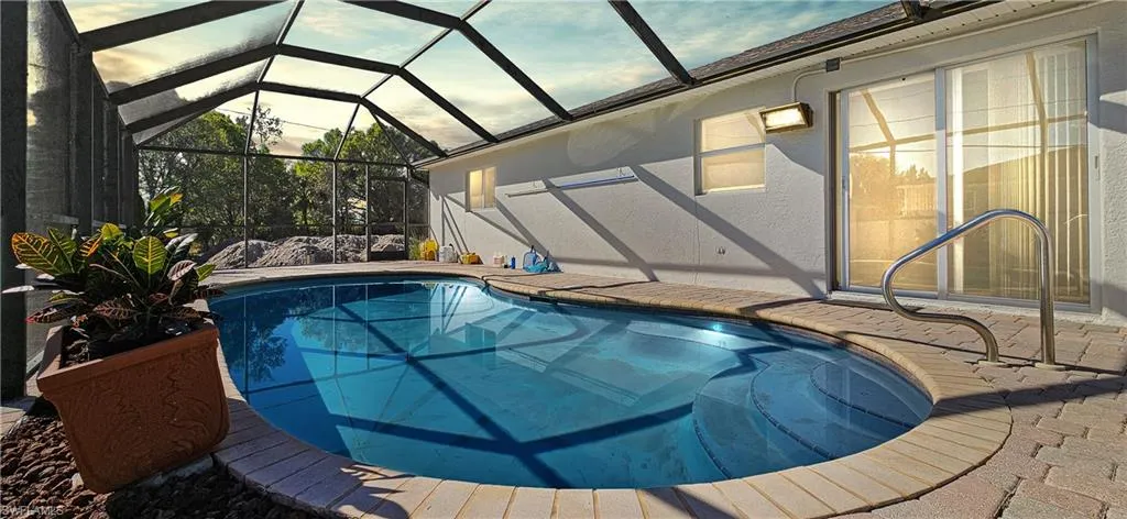 Pool at dusk with an outdoor pool, glass enclosure, a sunroom, and a patio
