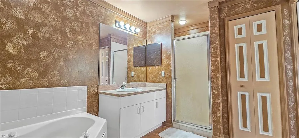 Bathroom featuring a stall shower, a bath, vanity, a closet, and wallpapered walls